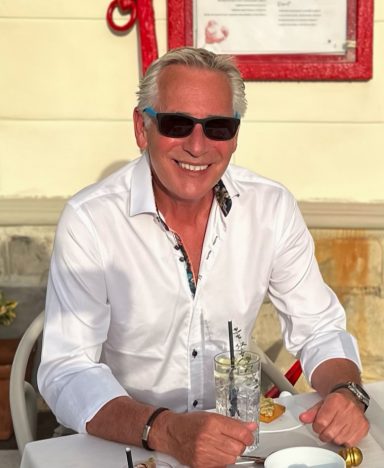 2024 Mature male lifestyle model wearing sunglasses seated at outdoor cafe